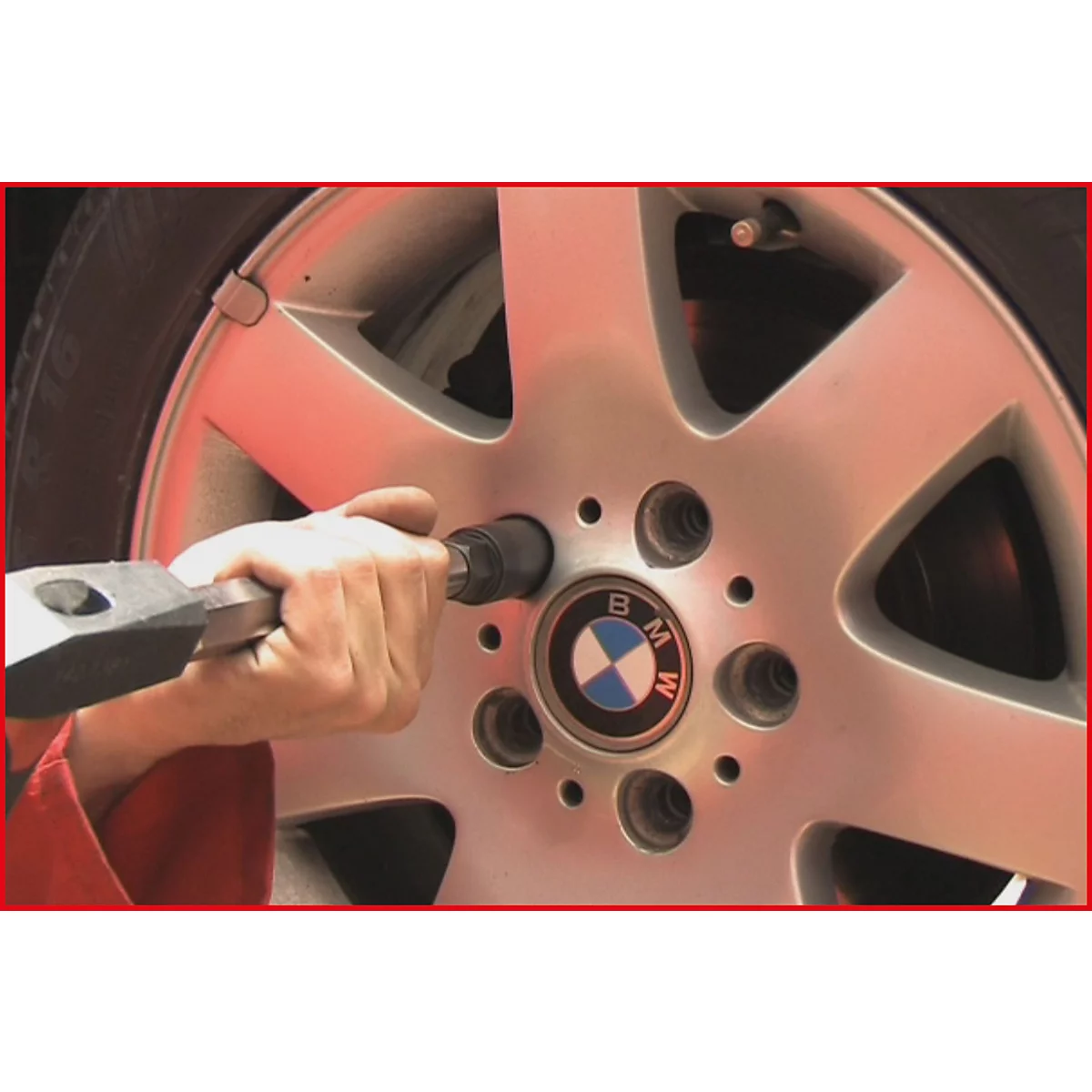 Nahaufnahme eines silbernen BMW-Rad, an dem eine Hand mit einem Werkzeug eine Schraube löst.